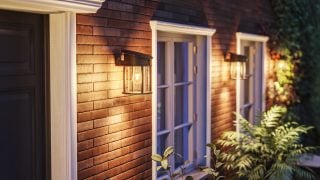 Mūsdienīga LED āra sienas lampa izgaismo rustisku koka ārējo apdari, demonstrējot energoefektīvus un laikapstākļu necaurlaidīgus apgaismojuma risinājumus mūsdienīgām mājas fasādēm un lieveņiem.