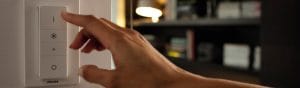 "Roku regulējot Philips viedo LED spilgtuma regulētāju, kontrolējot apkārtējo apgaismojumu mājīgā viesistabā ar grāmatu plauktiem."